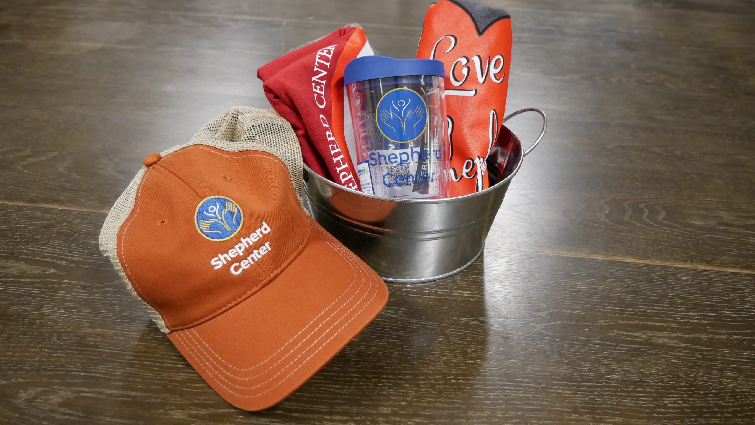 A metal bucket contains a plastic tumbler, red and black items, all featuring a 