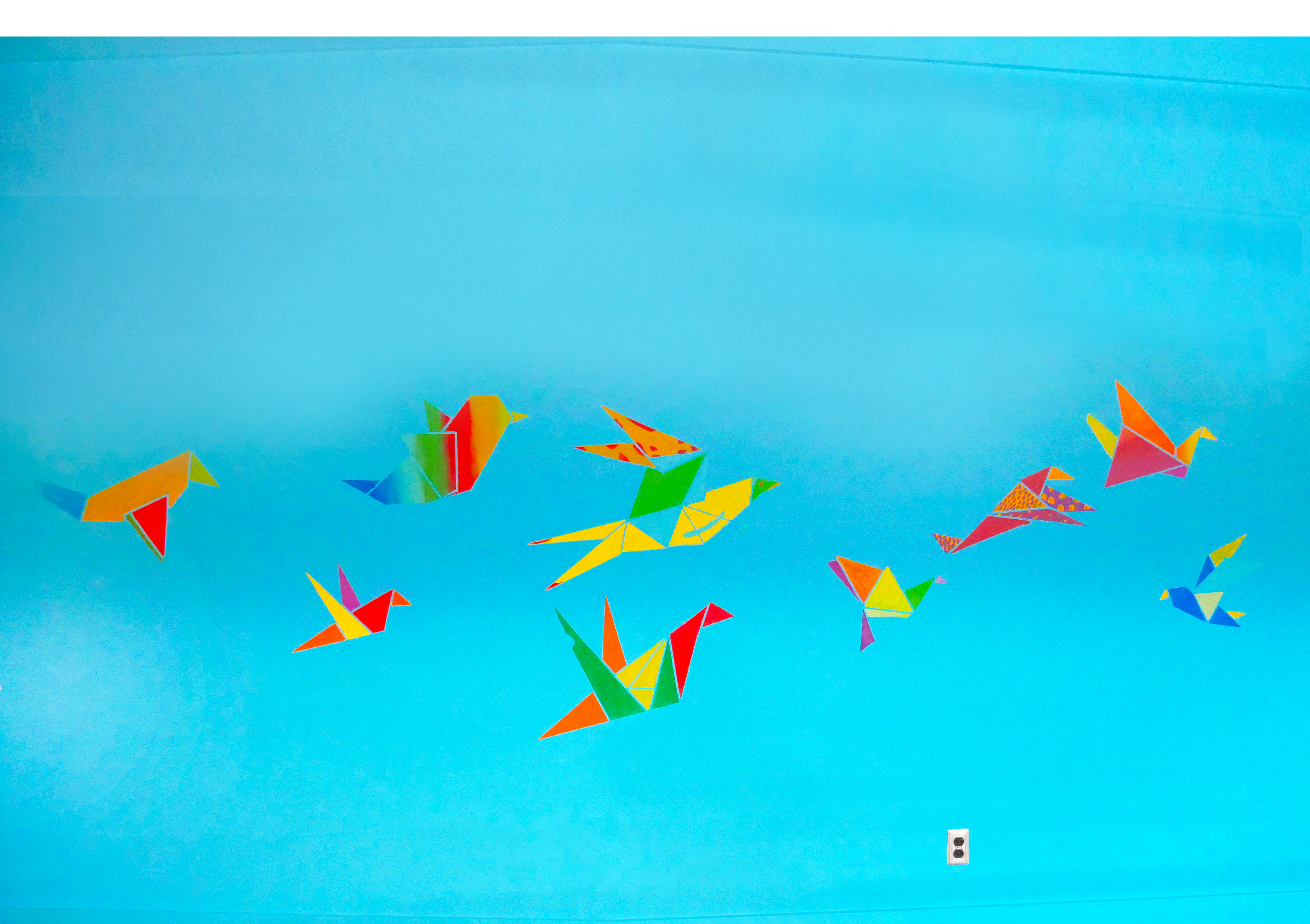 Colorful geometric origami birds in various sizes flying against a blue gradient background. The birds are made of vivid shapes in shades of red, yellow, green, and blue, creating a vibrant and abstract visual.