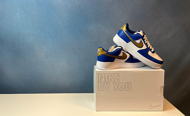 A pair of blue, white, and gold Nike sneakers rest on top of a white box labeled 